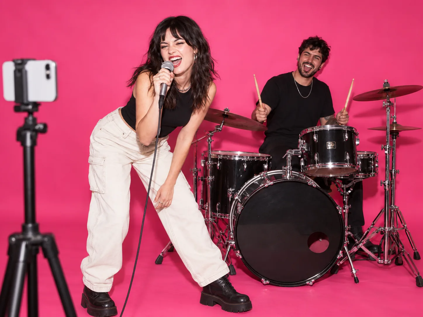 Two creators performing in a pink music-video studio while a phone records from the side